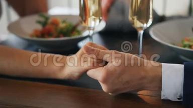 两只手的特写镜头男女放在桌上，配着闪闪发光的香槟酒杯和带食物的盘子。 浪漫